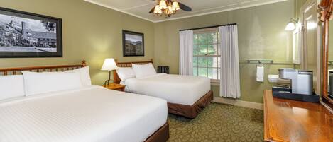 A hotel room with two beds, a ceiling fan, a framed picture, a window with curtains, a bathroom with a mirror and towel rack, and a wooden dresser.
