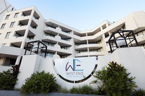 A multi-story building with balconies, a sign reading 'WEST END Central Apartments,' and surrounding greenery.