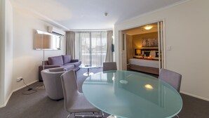 A modern hotel room with a glass table, comfortable seating, a flat-screen TV, and a view of the city through large windows. - West End Central Apartments (South Brisbane)