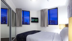 A hotel room with a bed, a television on the wall, and large windows with curtains. - West End Central Apartments (South Brisbane)