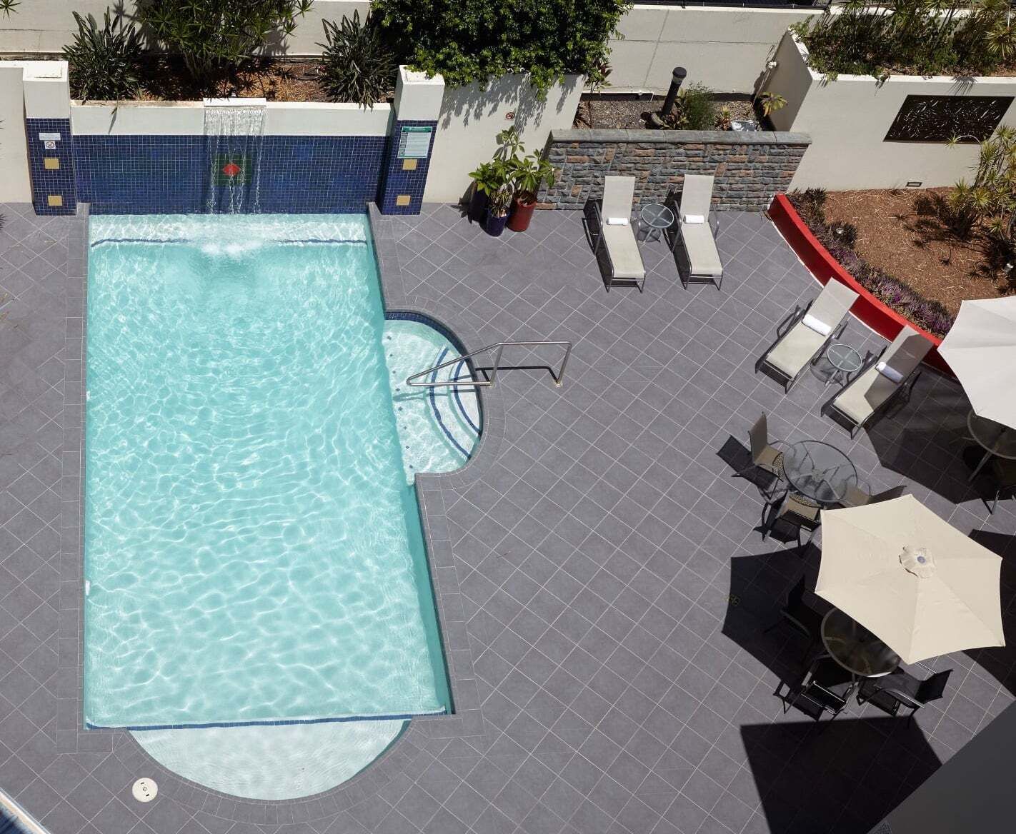 An outdoor swimming pool with a tiled deck, lounge chairs, and a small table with an umbrella.