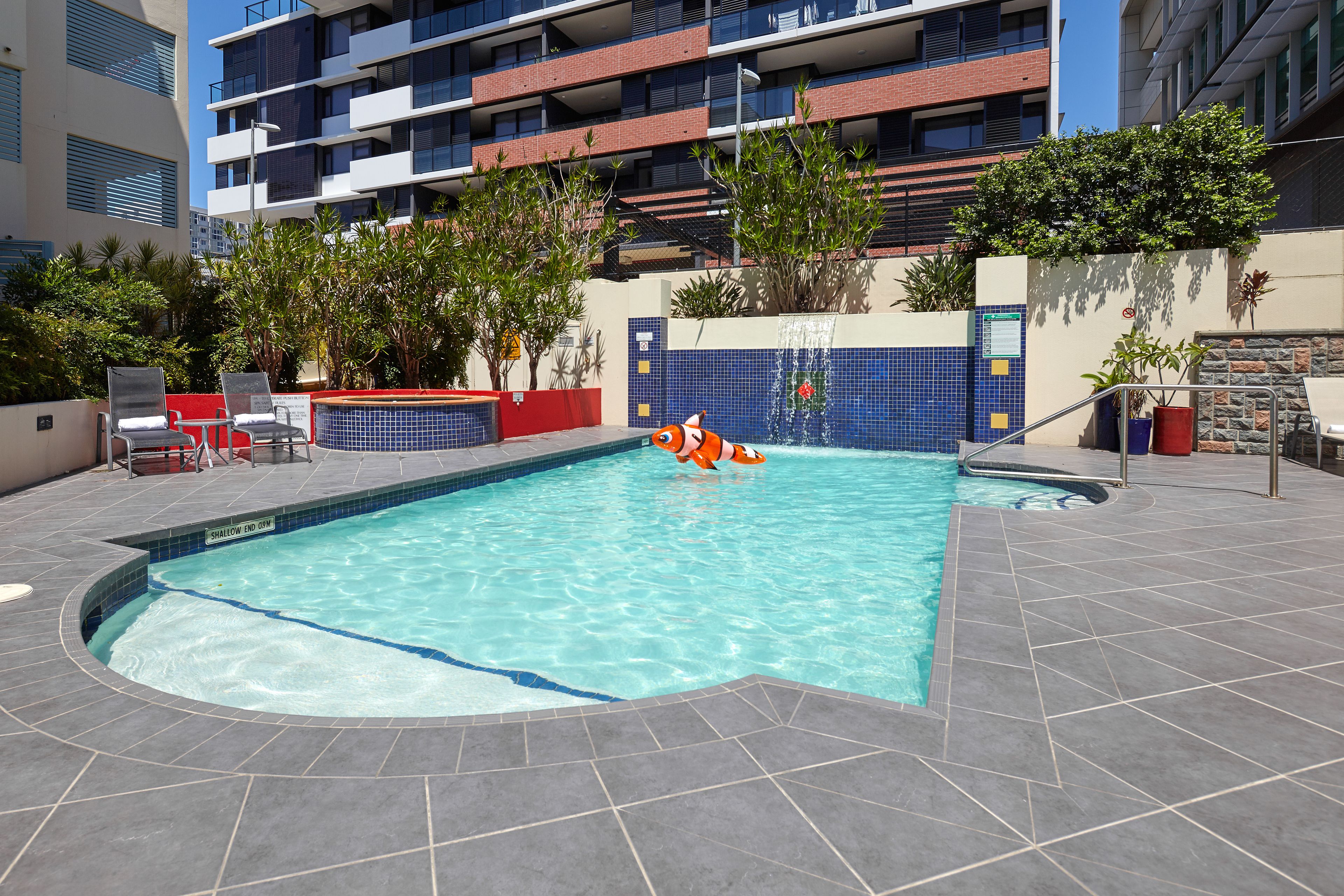 A swimming pool with a small inflatable shark, surrounded by lounge chairs and potted plants.