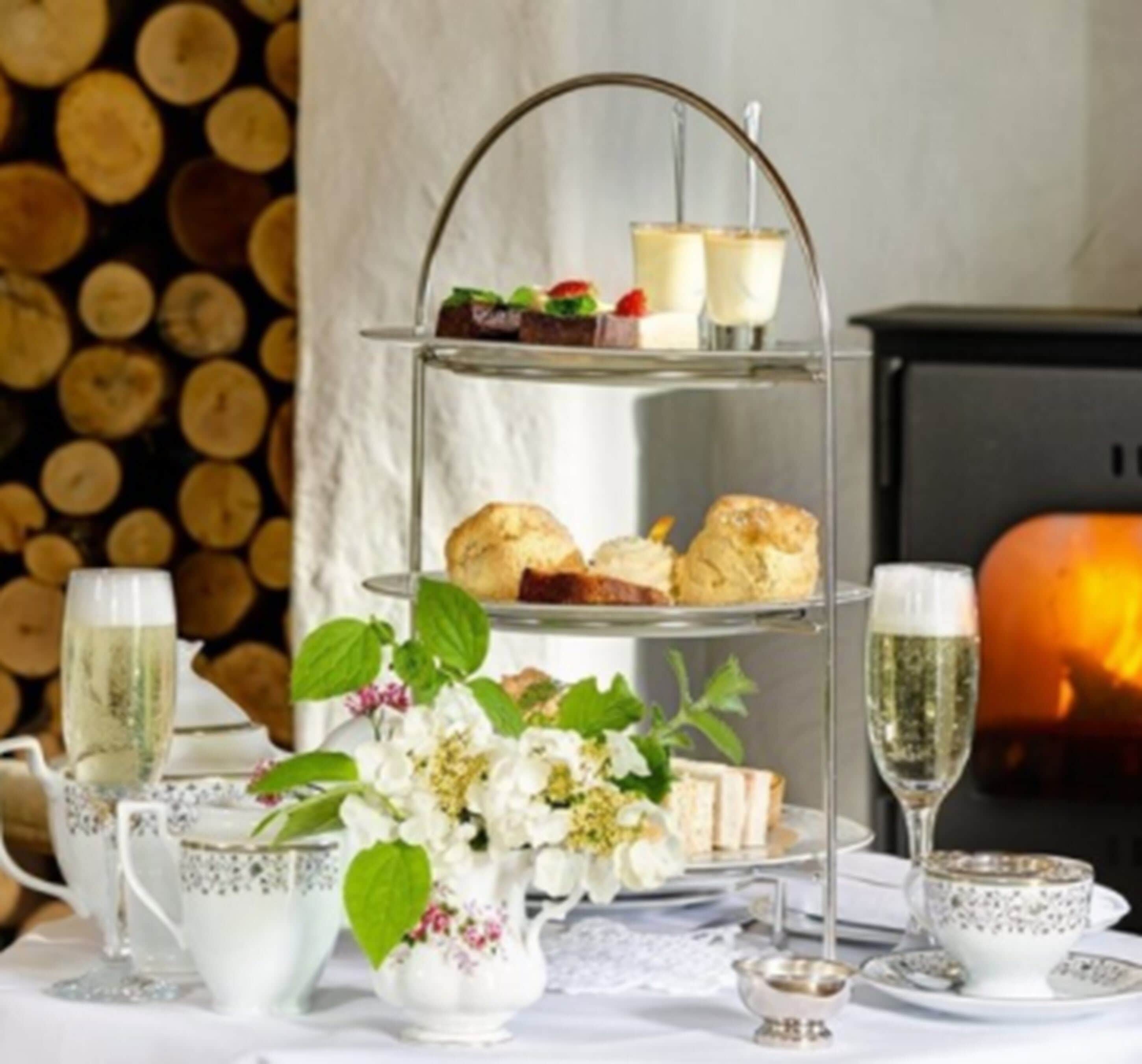 A three-tiered stand with pastries and a glass of champagne, a floral arrangement, and tea service on a table.