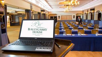 A laptop displaying the Ballygarry House Hotel and Spa Tralee sign, with a conference room in the background.