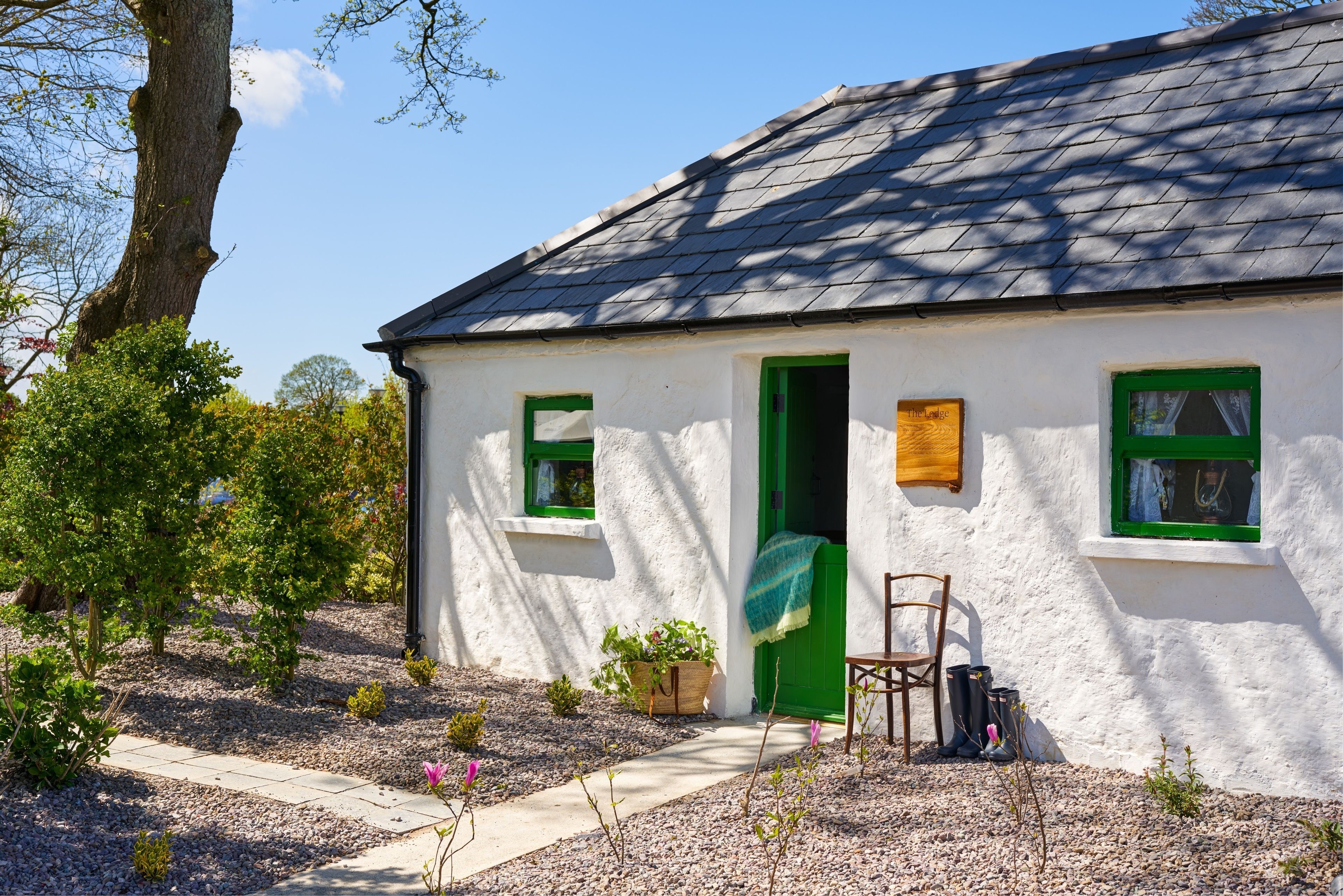 A white house with green doors and windows, a wooden door, and a chair outside.