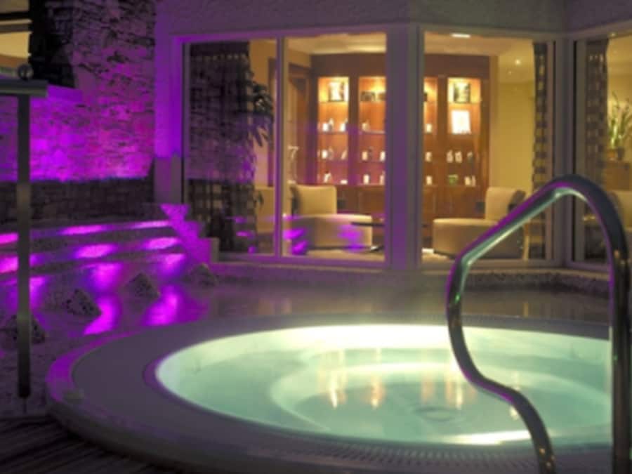 Zona de hidromasaje con recinto de vidrio, interior de madera y ambiente iluminado en morado.