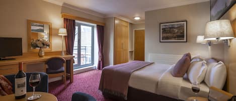 Una habitación de hotel con cama, escritorio, silla, televisor, ventana con cortinas y un cuadro en la pared.