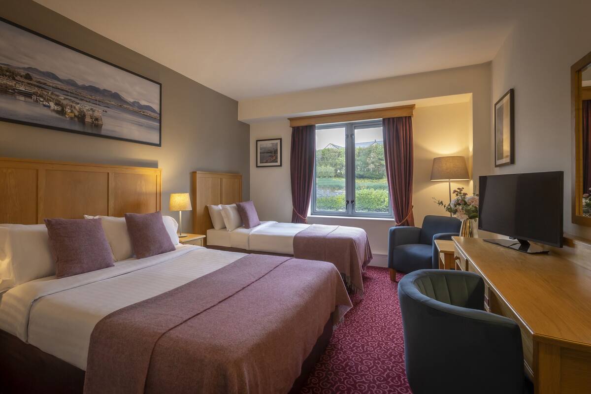 A hotel room with two beds, a desk, a TV, and a large window with curtains.