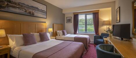 A hotel room with two beds, a desk, a TV, and a large window with curtains.
