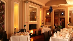 Un espace repas avec des tables dressées pour le dîner, une cheminée et un éclairage décoratif.