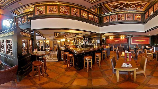 Un grand espace bar doté de nombreux tabourets et de tables, d’un comptoir central et d’un plafond haut orné de motifs complexes.