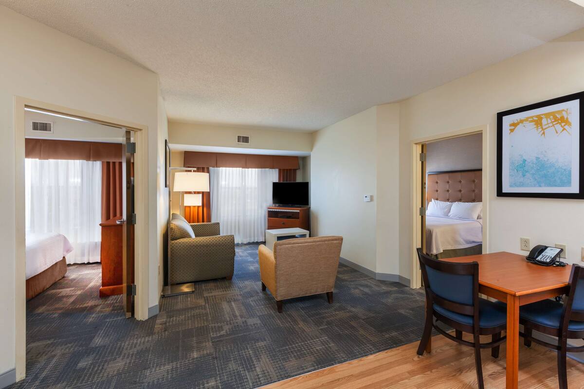 A hotel room with a bed, a desk, a chair, a sofa, a TV, and a painting on the wall.