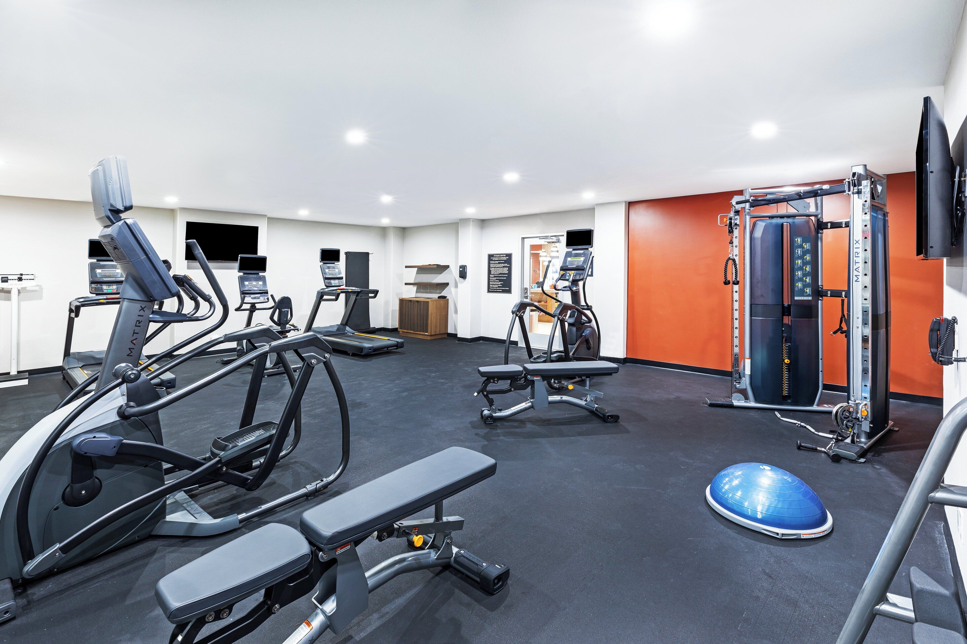 A gym with treadmills, elliptical machines, a bench press, and a weightlifting station.