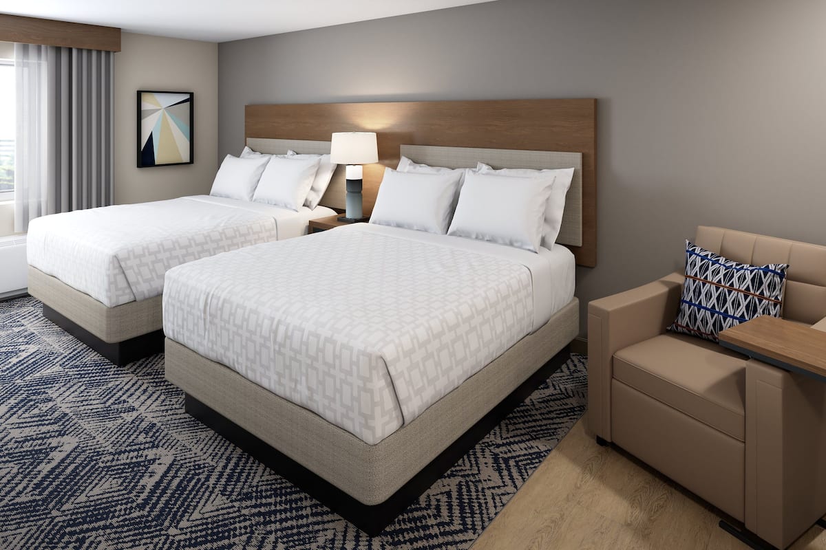 Ein Hotelzimmer mit zwei Betten, einem Schlafsofa, einem Nachttisch mit Lampe und einem gemusterten Teppich.
