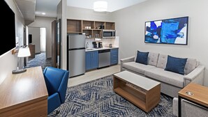 Une chambre d’hôtel moderne équipée d’une kitchenette, d’un canapé, d’une table basse et d’un tableau au mur.