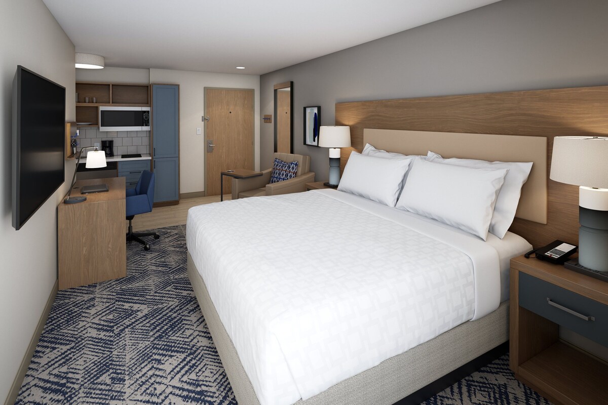 Ein Hotelzimmer mit einem großen Bett, einem Schreibtisch, einem Sessel, einer Mikrowelle, einer Kaffeemaschine und einem Fernseher.