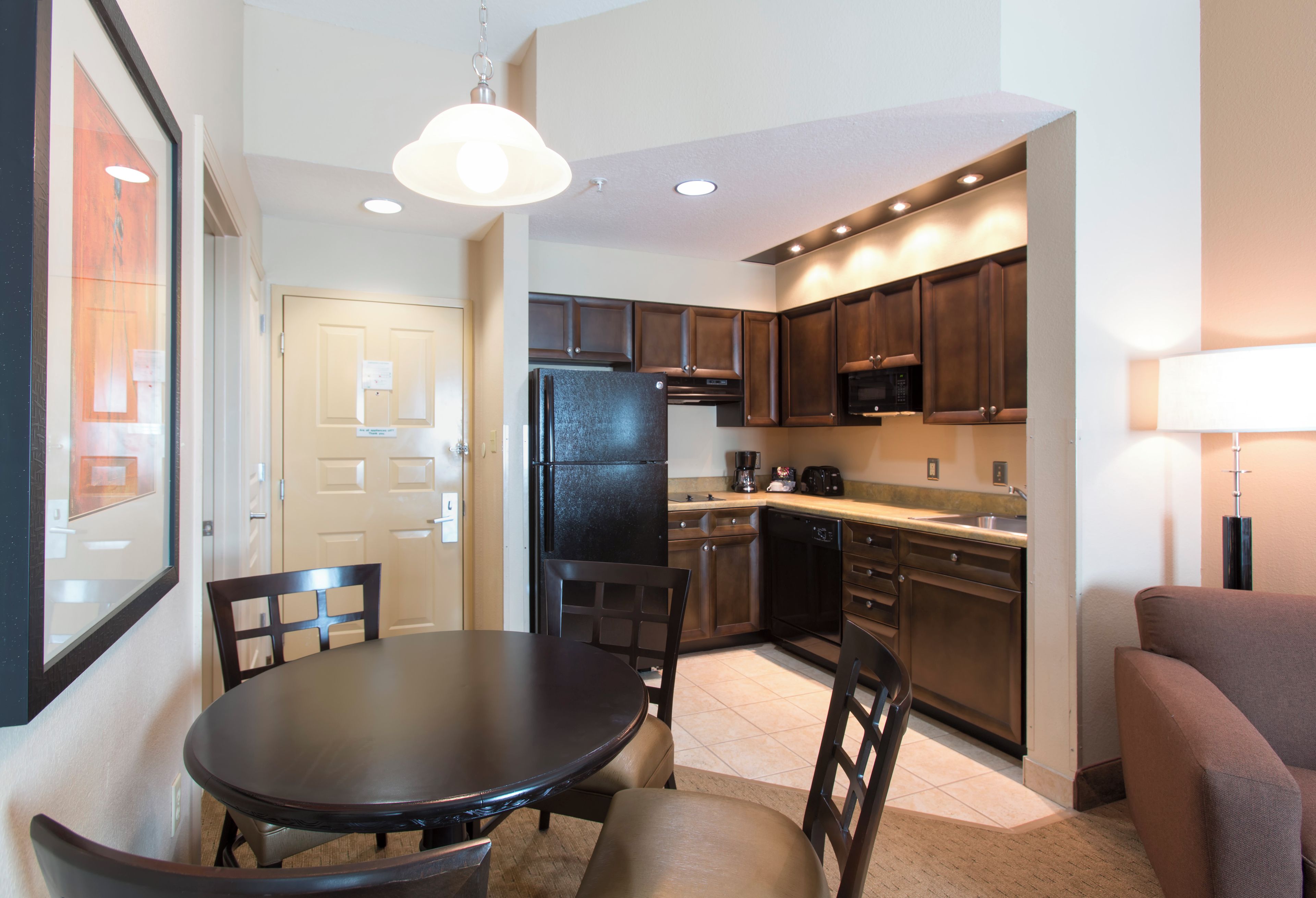 Una cocina compacta con armarios de madera oscura, un refrigerador negro y una mesa de comedor con sillas.