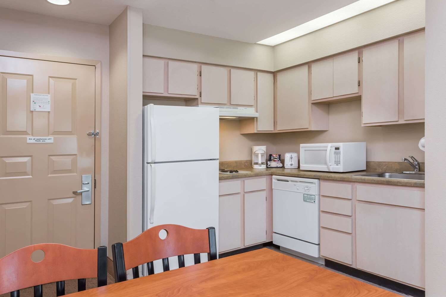 A compact kitchen with a refrigerator, microwave, coffee maker, and dishwasher. There is a wooden dining table with chairs.