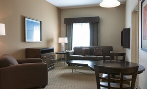 A hotel room with a sofa, a chair, a small table, a lamp, a TV, and a window with curtains. - The Palms at 8303 - Lake Buena Vista (Orlando)