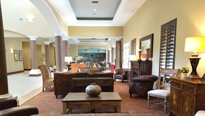 A spacious lobby with a central seating area featuring a leather sofa, a coffee table, and a wicker armchair. There is a wooden cabinet with a lamp on top, and a large mirror on the wall. The lobby has a high ceiling with recessed lighting and a patterned carpet. - Hawthorn Extended Stay by Wyndham Orlando (Orlando)