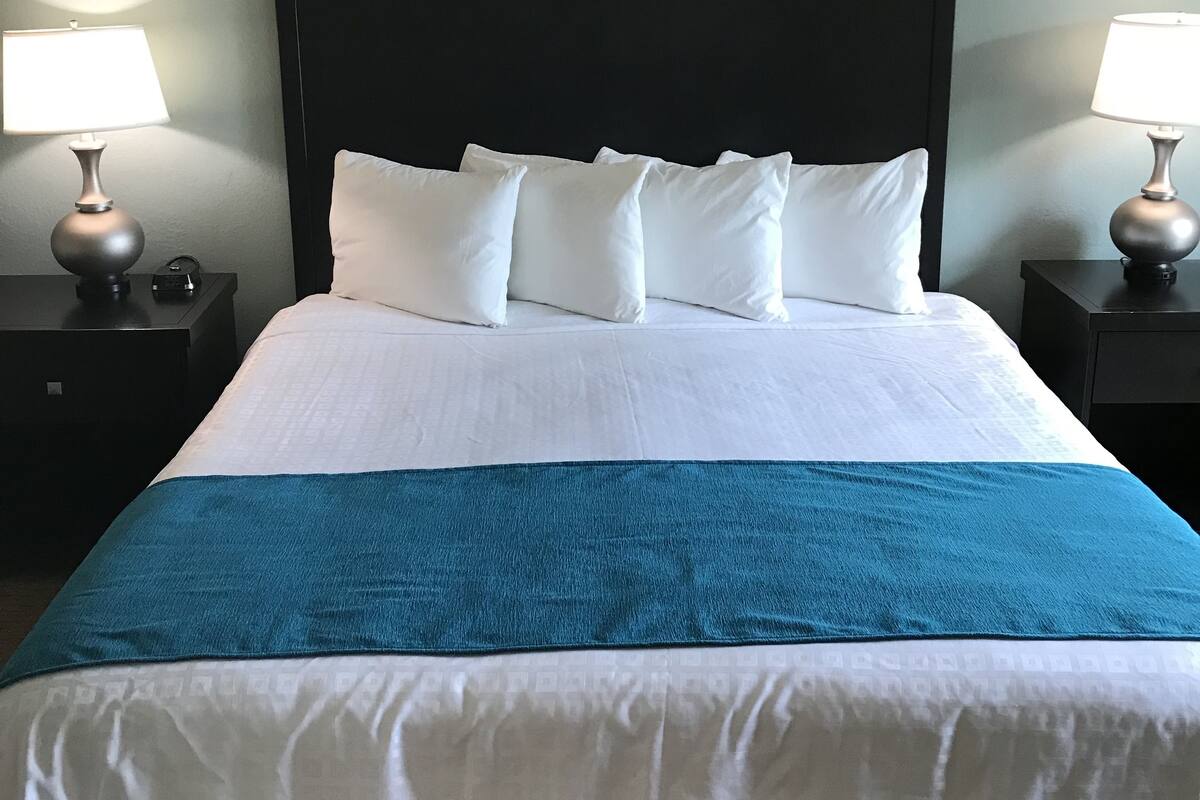 A neatly made bed with white and blue bedding, flanked by two nightstands with lamps and a clock.