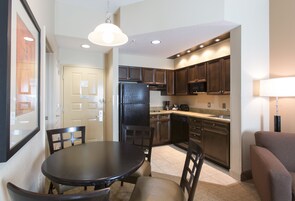 Una cocina compacta con armarios de madera oscura, un refrigerador negro y una mesa de comedor con sillas.