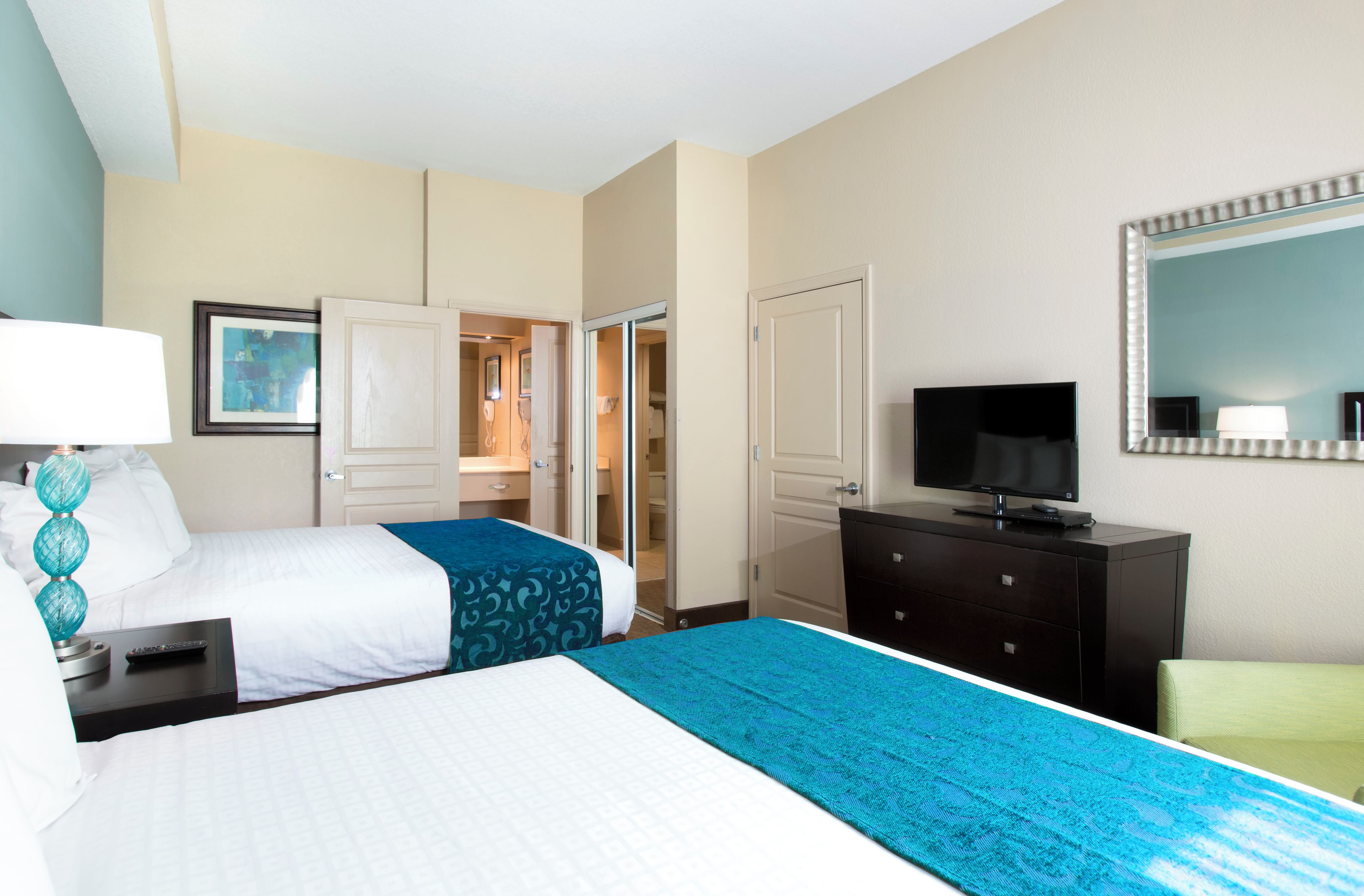 A hotel room with two beds, a TV, a dresser, and a mirror.