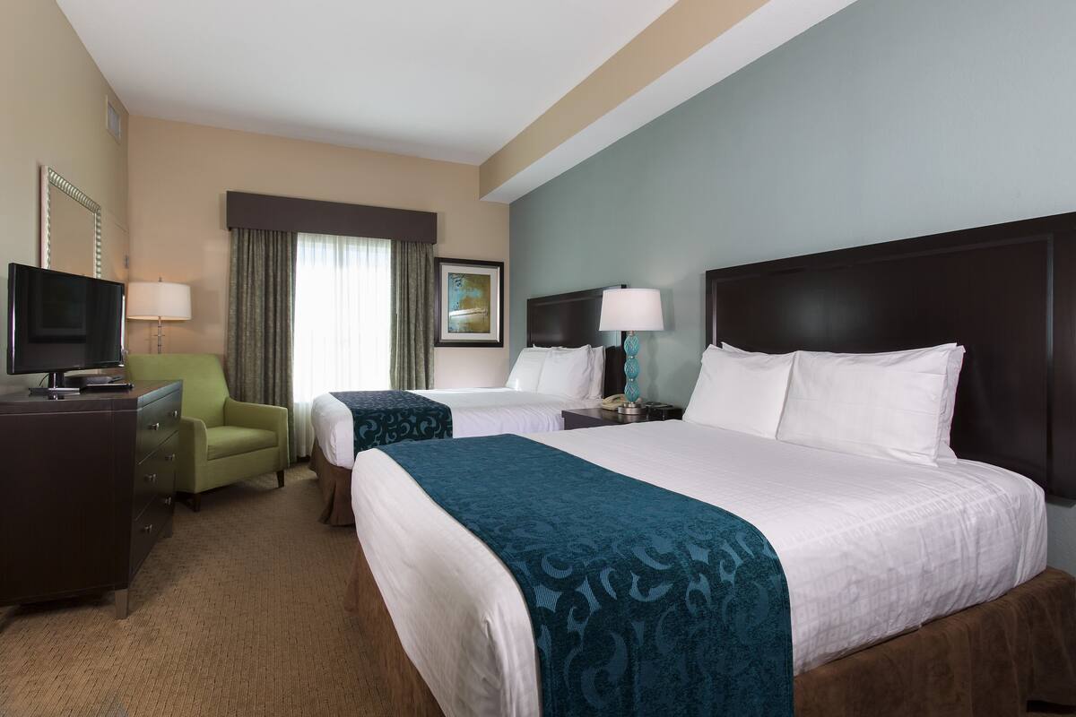 A hotel room with two beds, a desk, a TV, and a chair.