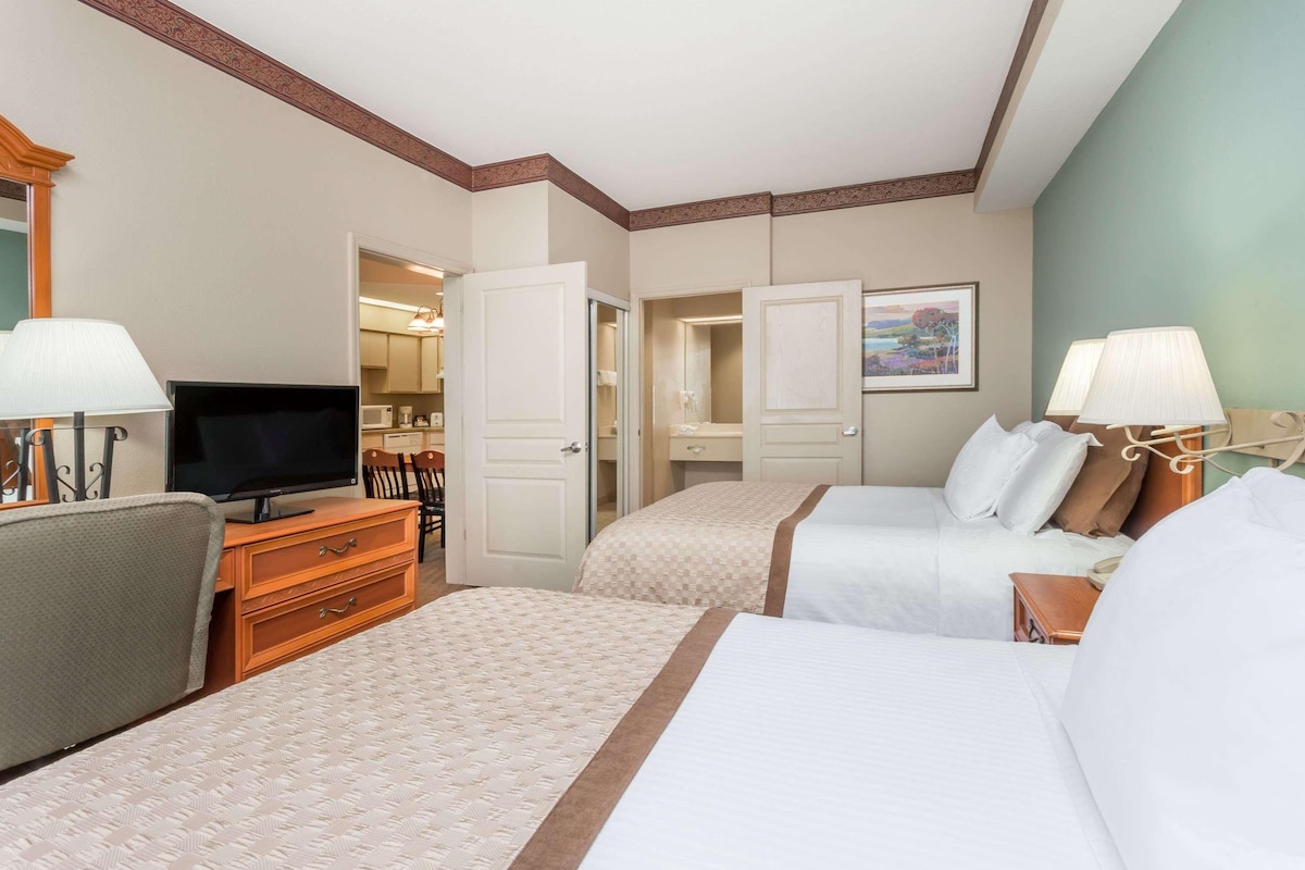 Quarto de hotel com duas camas, televisão, escrivaninha e uma cadeira.
