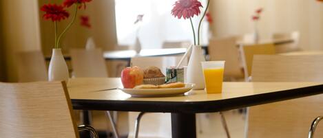 A dining table with a plate of food, a muffin, a glass of orange juice, and two red flowers in vases.