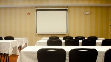 A conference room with tables and chairs, a projector screen, and a wall-mounted fire alarm.