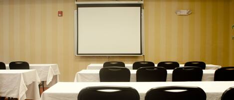Une salle de conférence équipée de tables et de chaises, d’un écran de projection et d’un détecteur d’incendie fixé au mur.