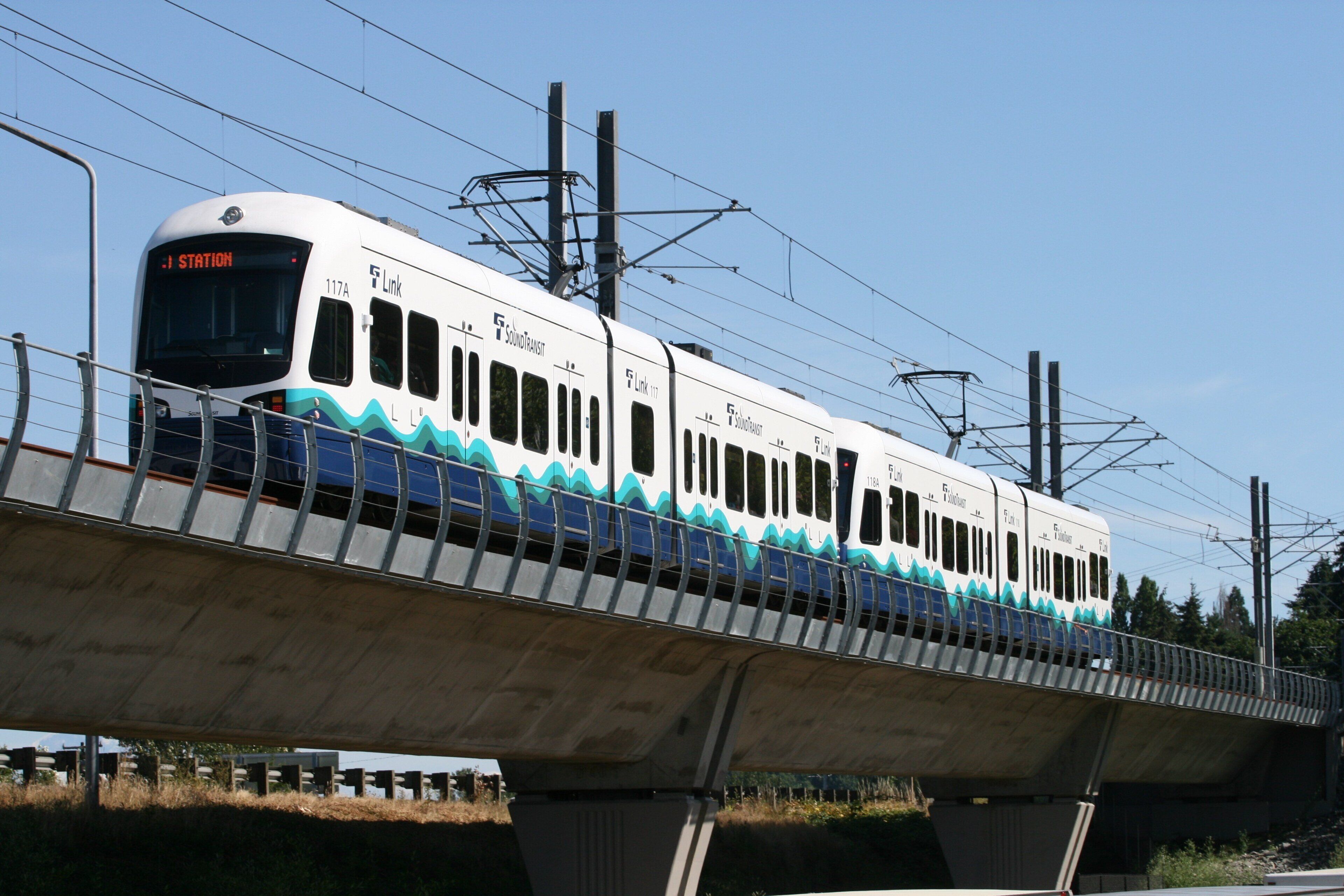 A white train with blue wave patterns on a bridge.