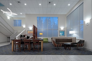 A hotel lobby with a reception desk, seating area, large windows, and a staircase. - Holiday Inn Express Hotel & Suites SeaTac by IHG (SeaTac)