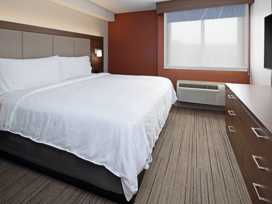 Habitación de hotel con una cama grande, televisor de pantalla plana, ventana con persianas y aire acondicionado integrado.