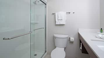 A modern bathroom with a glass shower enclosure, a white toilet, and a sink with a towel hanging on a rack.