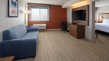 Quarto de hotel com sofá, escrivaninha, televisão de tela plana, cama e janela.