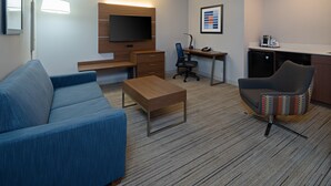 A hotel room with a blue sofa, a wooden desk, a computer, a chair, a television, and a kitchenette. - Holiday Inn Express Hotel & Suites SeaTac by IHG (SeaTac)