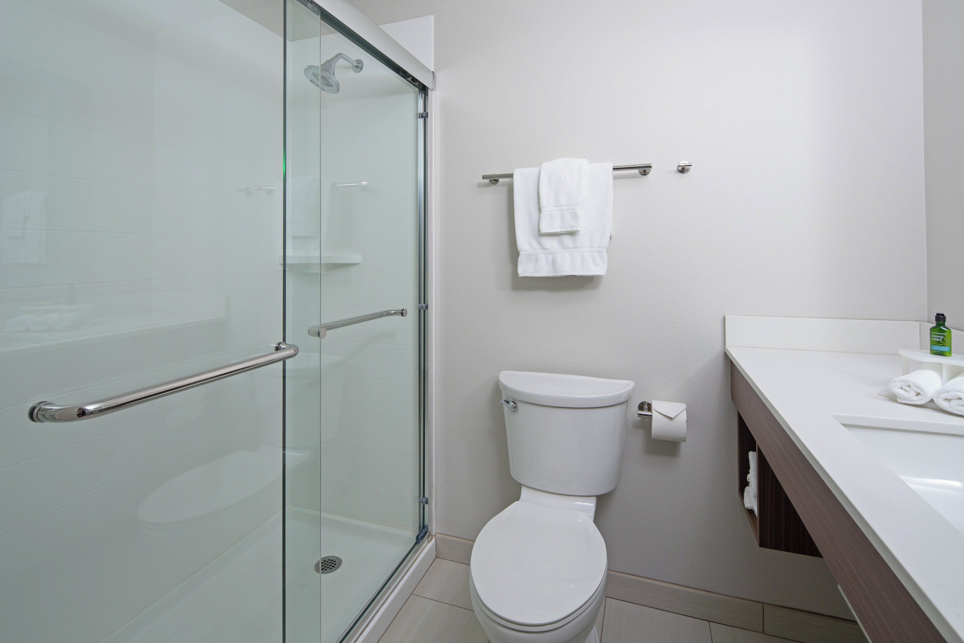A modern bathroom with a glass shower enclosure, a white toilet, and a white sink with a towel dispenser.