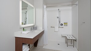 A modern bathroom with a wooden vanity, a large mirror, a shower with a glass door, and a small shelf with toiletries. - Holiday Inn Express Hotel & Suites SeaTac by IHG (SeaTac)