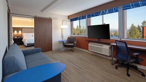 A hotel room with a sofa, a small table, a TV, a desk, and a chair. - Holiday Inn Express Hotel & Suites SeaTac by IHG (SeaTac)