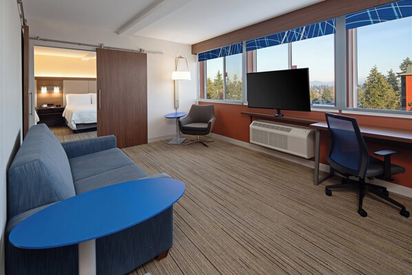 A hotel room with a sofa, a small table, a TV, a desk, and a chair. - Holiday Inn Express Hotel & Suites SeaTac by IHG (SeaTac)
