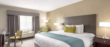 A hotel room with a large bed, two bedside lamps, a desk with a chair, and a window with curtains.