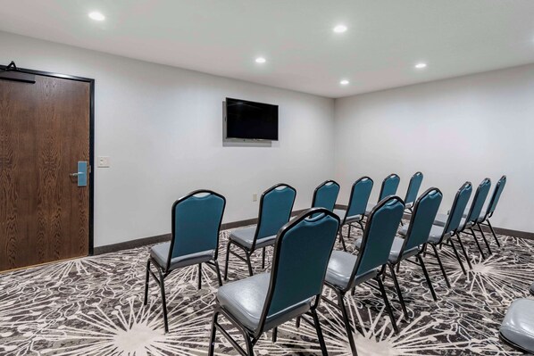Un salón de conferencias con una fila de sillas color turquesa, una puerta de madera y un televisor montado en la pared.