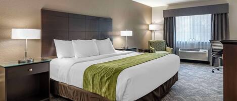 A hotel room with a large bed, two bedside tables with lamps, a chair, and a window with curtains.