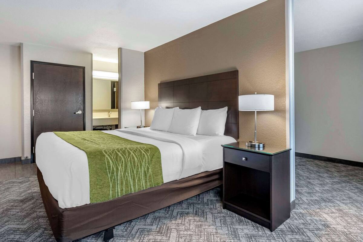 Habitación de hotel con una cama grande, dos mesitas de noche con lámparas, una puerta y un espejo.