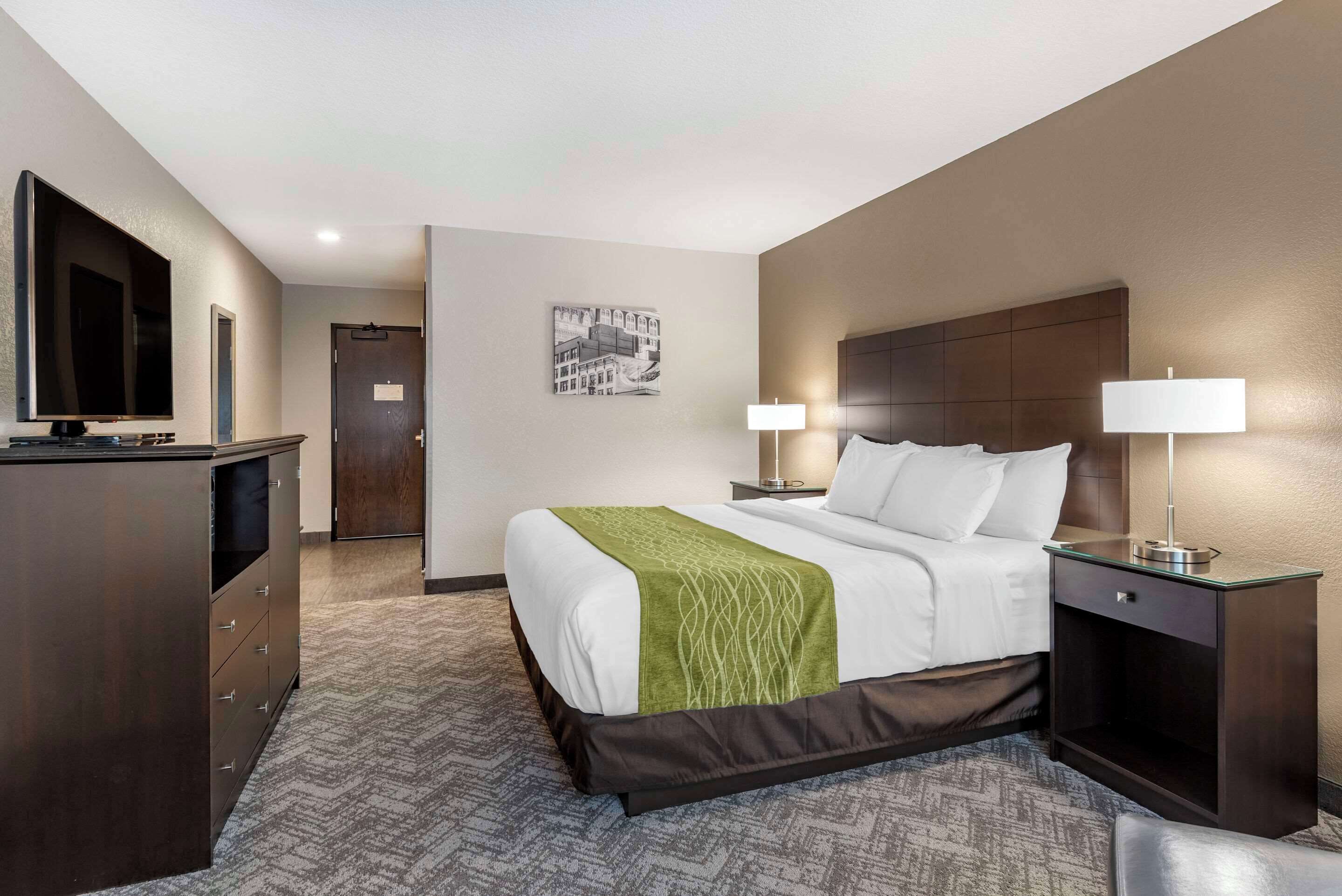 Une chambre d’hôtel avec un lit, des lampes de chevet, une télévision, un bureau et une porte.