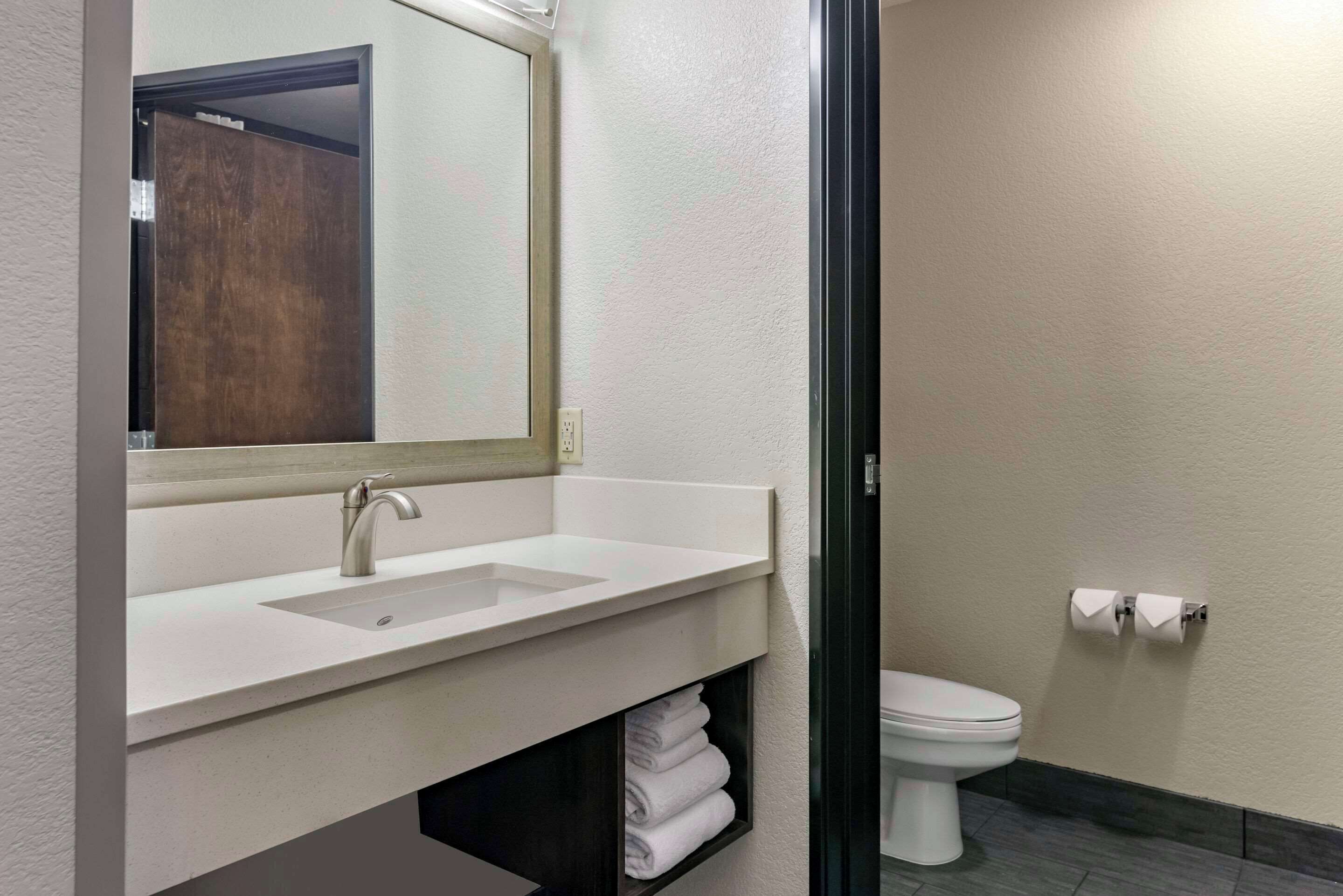 A modern bathroom with a white sink, a mirror, and a toilet.