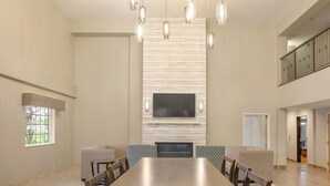 A spacious dining area with a long wooden table, green cushioned chairs, and a modern chandelier.