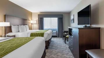 A hotel room with two beds, a desk, a TV, and a window with curtains.